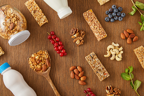 Top view of food composition of berries, nuts, cereal bars and bottles of yogurt and milk on wooden background