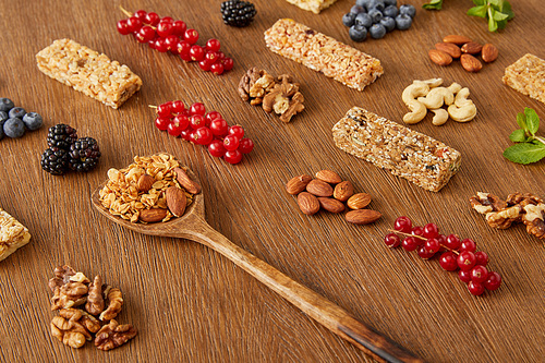 Berries, nuts, cereal bars and spatula with granola on wooden background