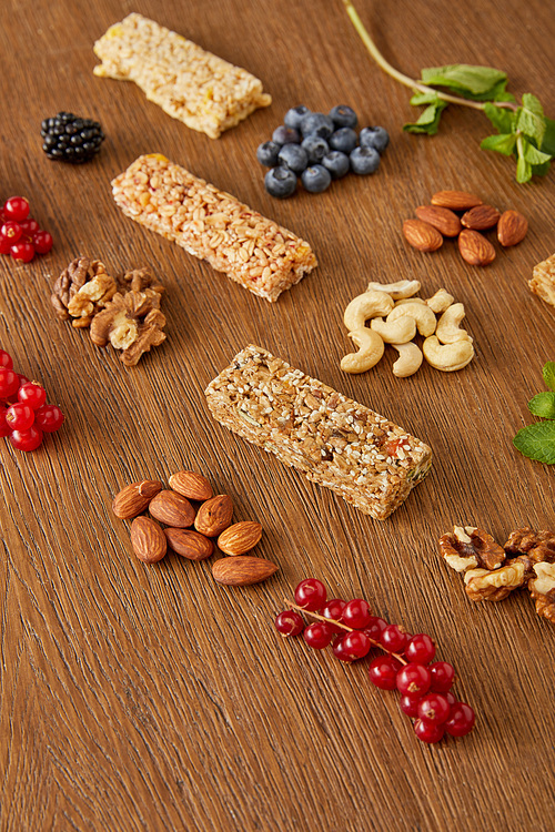 Selective focus of berries, nuts, cereal bars, mint on wooden background