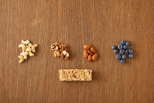 Top view of walnuts, almonds, cashews, blueberries and cereal bar on wooden background