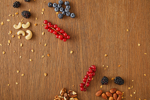 Top view of blueberries, redcurrants, walnuts, almonds, cashews and oat flakes on wooden background