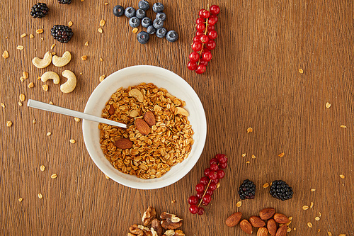 Top view of bowl with granola and blueberries, redcurrants, walnuts, almonds, cashews on wooden background