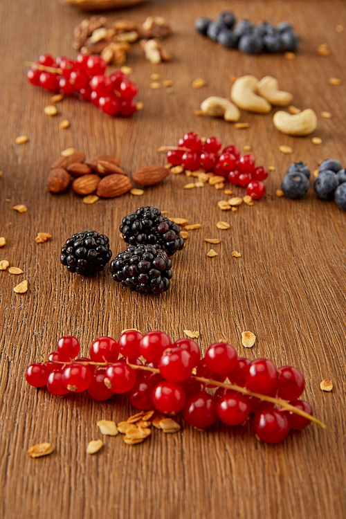 Selective focus of redcurrants, blueberries, oat flakes and nuts on wooden background