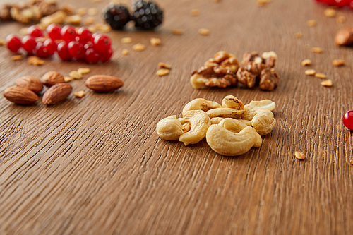 Selective focus of cashews with almonds, walnuts, redcurrants, blackberries on wooden background