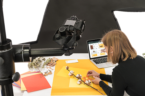 photographer making composition with cotton flower and accessories for photo shooting with camera and laptop