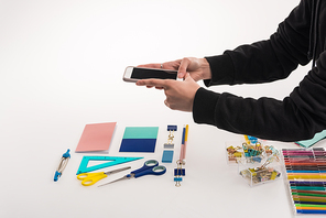 cropped view of photographer making flat lay with office supplies for commercial photo shooting on smartphone