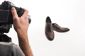 cropped view of male photographer making commercial photo shoot of male shoes on white