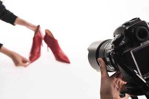 cropped view of commercial photographers making commercial photo shoot of female red heel shoes on white