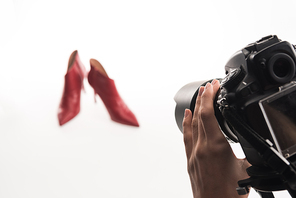 cropped view of female photographer making commercial photo shoot of female red heel shoes on white