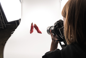 cropped view of commercial photographer making commercial photo shoot of female red heel shoes on white