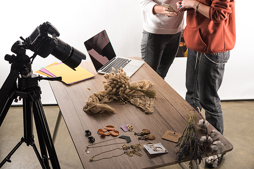 cropped view of two commercial photographers working with accessories, digital camera, laptop and smartphone
