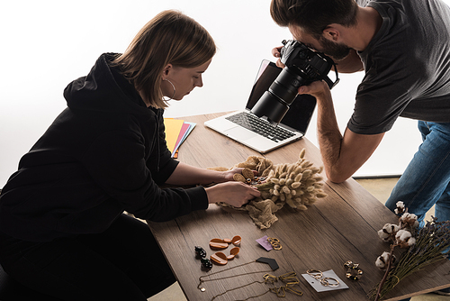 two commercial photographers take picture of composition with flora and jewelry on digital camera