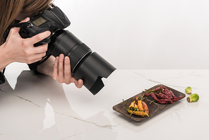 cropped view of female photographer making food composition for commercial photography and taking photo on digital camera on white