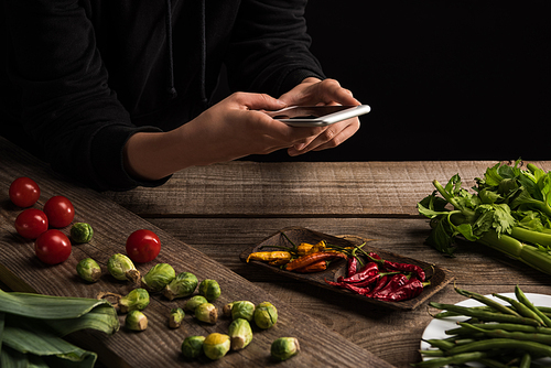 cropped view of photographer making food composition for commercial photography on smartphone on wooden table