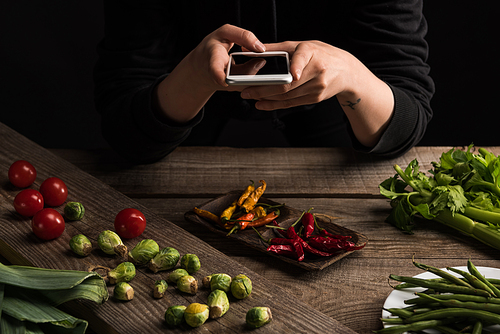 cropped view of professional photographer making food composition for commercial photography on smartphone on wooden table