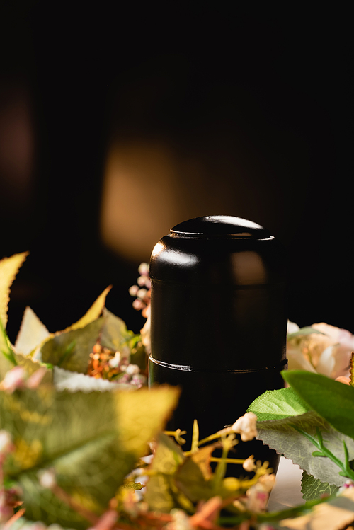 bouquet and urn with ashes on black background, funeral concept