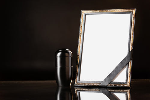 urn with ashes, mirror with black ribbon on black background, funeral concept