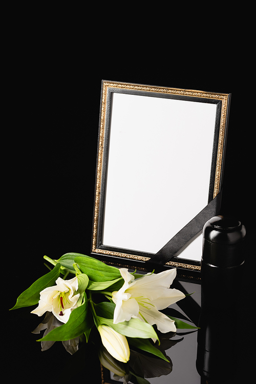 flowers, mirror with black ribbon and urn with ashes on black background, funeral concept