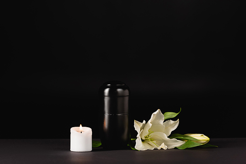 lily, candle and urn with ashes on black background, funeral concept