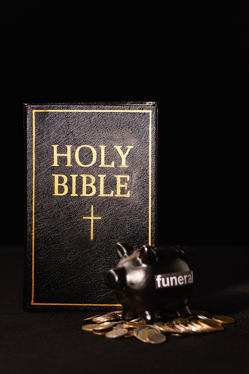 piggy bank with coins and holy bible on black background, funeral concept