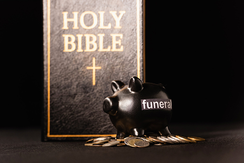 piggy bank with coins and holy bible on black background, funeral concept