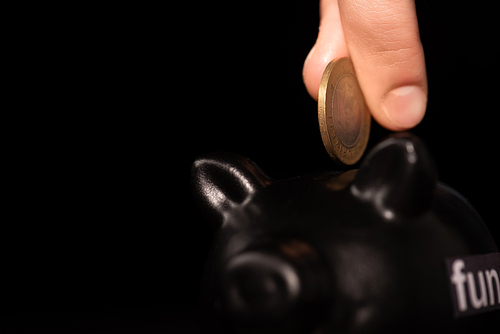 cropped view of man putting coin in piggy bank on black background, funeral concept