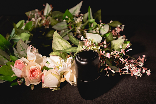 rose bouquet and urn with ashes on black background, funeral concept