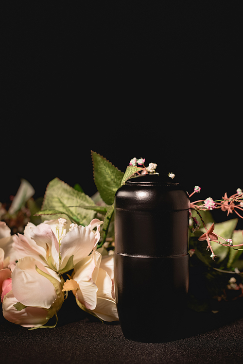 rose bouquet and urn with ashes on black background, funeral concept