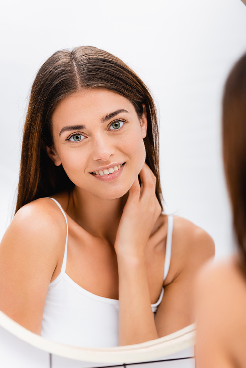 young woman with perfect skin smiling near mirror in bathroom, blurred foreground