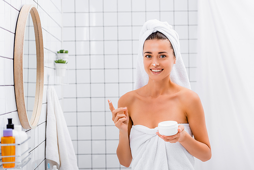 cheerful woman with face cream on nose smiling at camera in bathroom