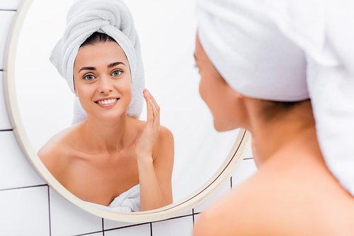 cheerful woman applying facial scrub near mirror in bathroom, blurred foreground