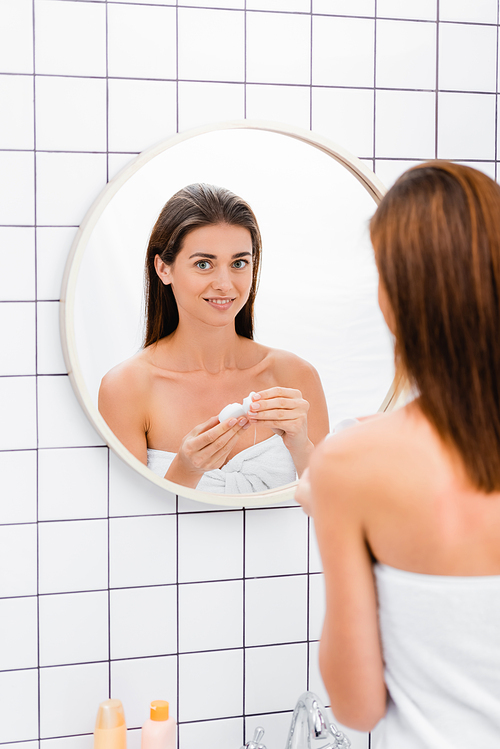 smiling woman holding dental floss near mirror in bathroom, blurred foreground