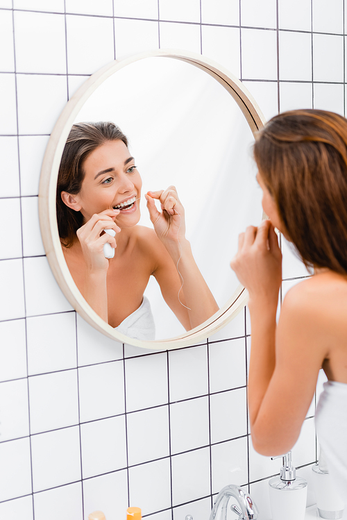 young woman flossing teeth near mirror in bathroom, blurred foreground