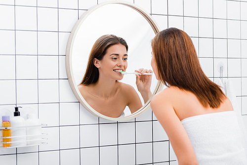 young woman looking in mirror while brushing teeth in bathroom