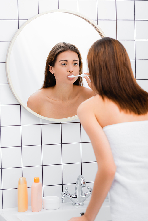 young woman brushing teeth while looking in mirror in bathroom