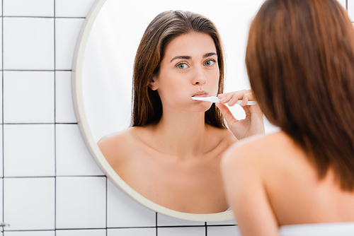 young woman brushing teeth near mirror in bathroom, blurred foreground