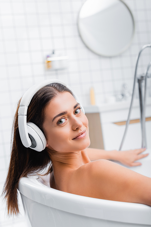 happy young woman  while taking bath and listening music in wireless headphones