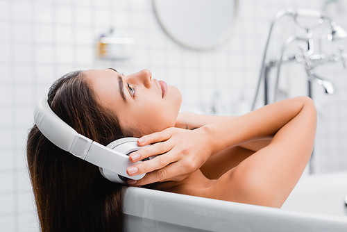 young woman touching wireless headphones while taking bath and listening music