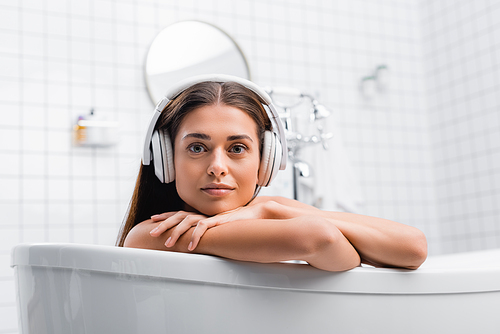 young woman listening music in wireless headphones while taking bath and 