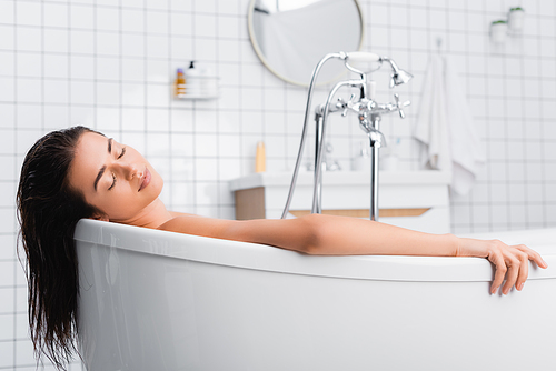 young woman with closed eyes relaxing while taking bath at home