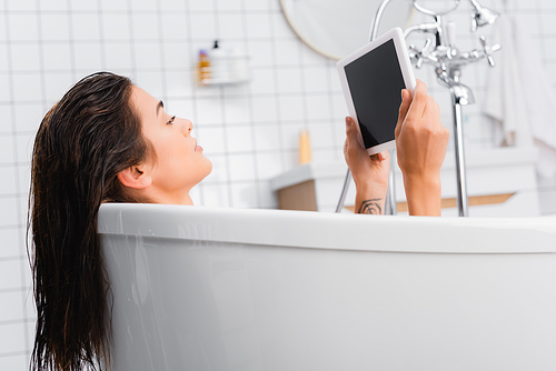 young woman taking bath and holding digital tablet with blank screen