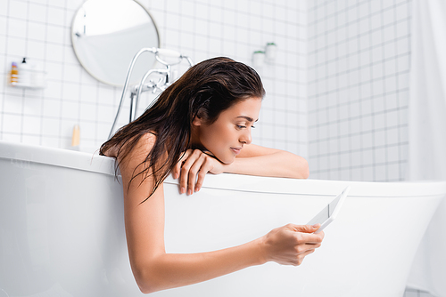 smiling woman using digital tablet while taking bath at home