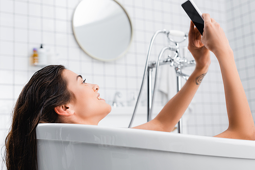 young smiling woman taking selfie while relaxing in bathtub