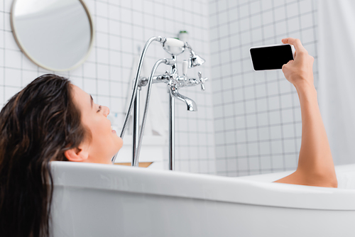 young woman taking selfie on smartphone in bathtub, blurred foreground