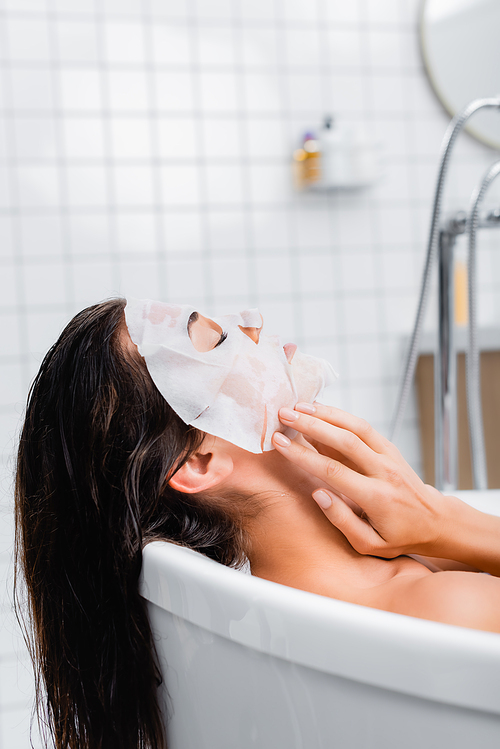 young woman touching face mask while taking bath at home