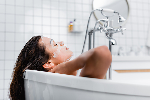 young woman in face mask relaxing with closed eyes in bathtub, blurred background