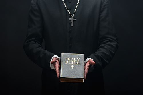 cropped view of catholic priest holding holy bible isolated on black
