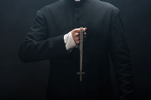 cropped view of catholic priest holding necklace with silver cross isolated on black