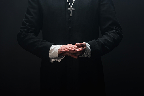 cropped of catholic priest standing with folded hands isolated on black
