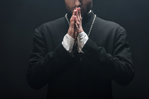 cropped view of young catholic priest praying isolated on black